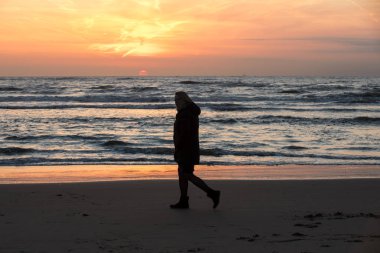 Katwijk, Hollanda - 23 Nisan 2017: Katwijk plajda günbatımında yürüyen kadın. Hollanda