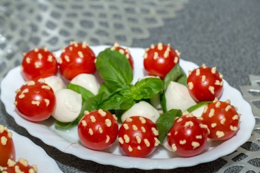 Beyaz tabakta mayonez, fesleğen ve mozarella ile kokteyl domatesleri.