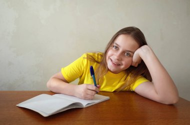 Gri duvarlı, çocuklu, eğitim ve öğrenim konseptli ahşap masaüstüne yerleştirilmiş mutlu kız yazıları