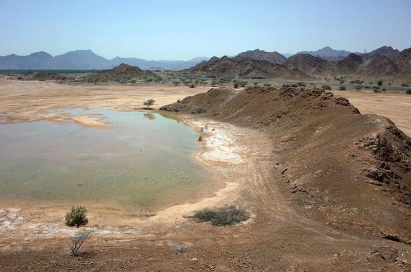 Arabian peninsula landscape with cracked mud, puddle and dry mountains in Fujairah, United Arab Emirates