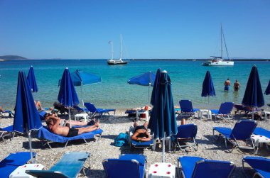 Pythagorion, Samos Adası, Yunanistan - 14 Mayıs 2018: İnsanlar Ege Denizi 'nin turkuaz suyunda demirlemiş yelkenliyle plajda dinleniyor