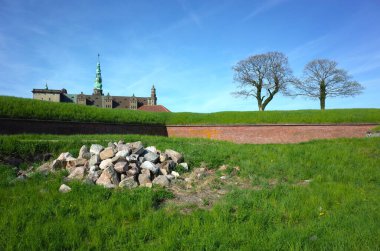 Helsingor, Danimarka - 06 Mayıs 2018: Kronborg kalesinin savunma duvarının arkasında büyüyen iki ağaç, yeşil çimenler ve ön planda taş yığını