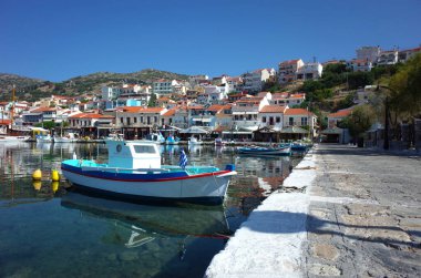 Pisagor, Samos Adası, Yunanistan - 15 Mayıs 2018: Körfezdeki geleneksel renkli Yunan balıkçı teknesi ve tepenin üzerindeki Pisagor köyü