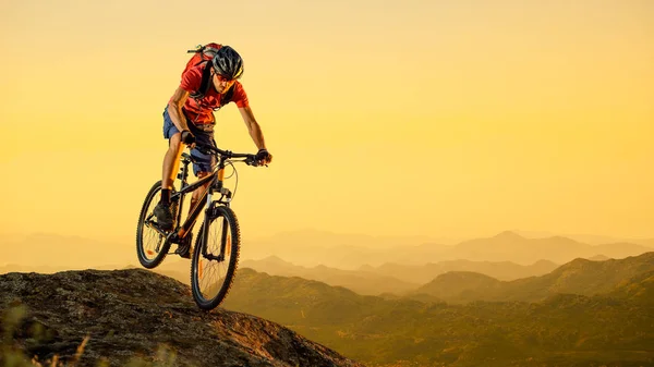Ποδηλάτης στο κόκκινο ιππασίας το ποδήλατο κάτω από το βράχο στο ηλιοβασίλεμα. Extreme Sport και έννοια ποδήλατο Enduro. — Φωτογραφία Αρχείου
