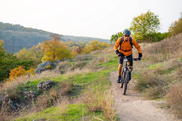 Cyclist in Orange Riding the Mountain Bike on the Autumn Rocky Enduro Trail. Extreme Sport and Enduro Biking Concept.