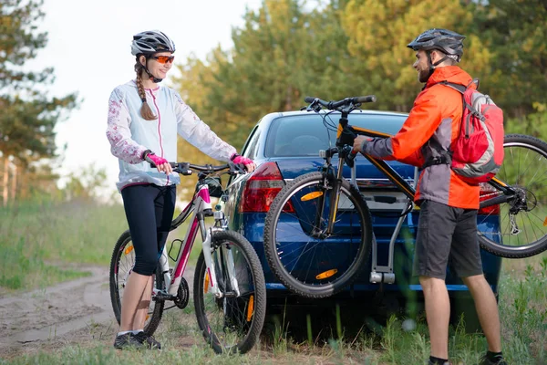 Junges Paar demontiert Mountainbikes vom Fahrradständer am Auto. Erlebnis- und Familienreisekonzept. — Stockfoto