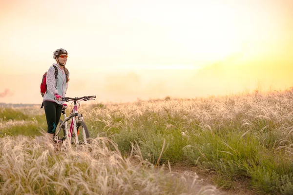 Junge Frau auf Mountainbikes im schönen Feld von Federgras bei Sonnenuntergang. Abenteuer und Reisen. — Stockfoto