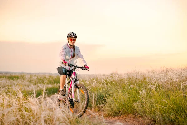 Junge Frau auf Mountainbikes im schönen Feld von Federgras bei Sonnenuntergang. Abenteuer und Reisen. — Stockfoto