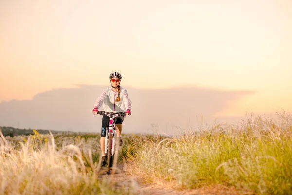 Giovane donna a cavallo mountain bike nel bellissimo campo di erba piuma al tramonto. Avventura e viaggi . — Foto Stock