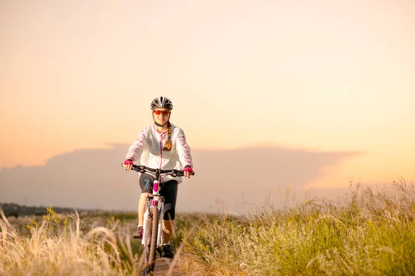 Ung kvinna Rider mountainbikes i fältet vacker fjäder gräs vid solnedgången. Äventyr och resor. — Stockfoto