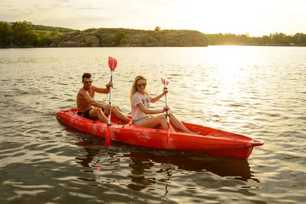 年轻夫妇在美丽的河或湖上划船独木舟在傍晚日落 — 图库照片
