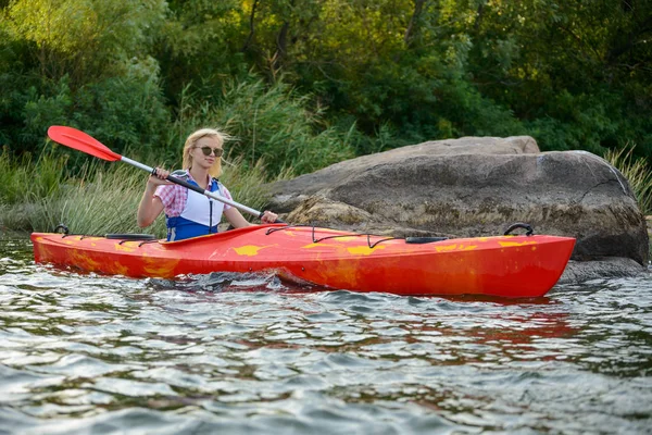 Jeune femme pagayant kayak sur belle rivière ou lac parmi les pierres à la soirée — Photo