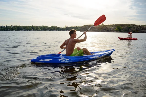 Junger Mann paddelt Kajak auf dem schönen Fluss oder See unter dramatischem Abendhimmel bei Sonnenuntergang — Stockfoto