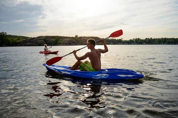 Jeune homme pagayant kayak sur la belle rivière ou le lac sous le ciel dramatique du soir au coucher du soleil — Photo