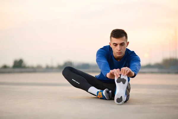 Joven corredor masculino estirándose y preparándose para correr al atardecer. Concepto de estilo de vida saludable y deporte . —  Fotos de Stock