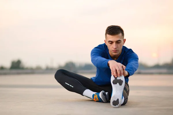 Joven corredor masculino estirándose y preparándose para correr al atardecer. Concepto de estilo de vida saludable y deporte . —  Fotos de Stock