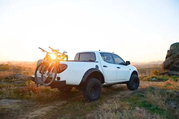 Camioneta todoterreno con bicicletas en el cuerpo en las montañas al atardecer. Concepto de viaje de aventura y coche . — Foto de Stock