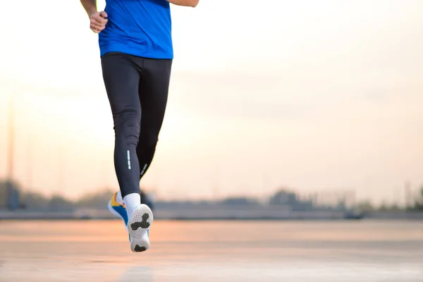 Gros plan sur les jambes des hommes sportifs qui courent au coucher du soleil. Mode de vie sain et concept sportif . — Photo