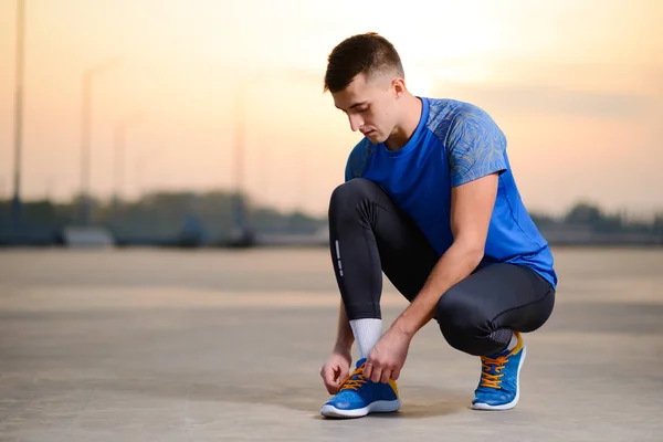 Mladý muž sportovec vázání běžecké boty a příprava na městské běžet západem slunce. Zdravý životní styl a Sport koncept. — Stock fotografie