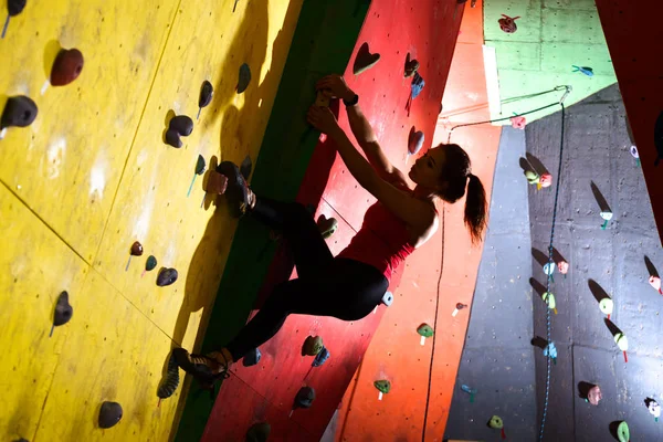 Giovane donna attiva che bouldering sulla roccia artificiale variopinta nella palestra di arrampicata. Sport estremi e concetto di arrampicata indoor — Foto Stock