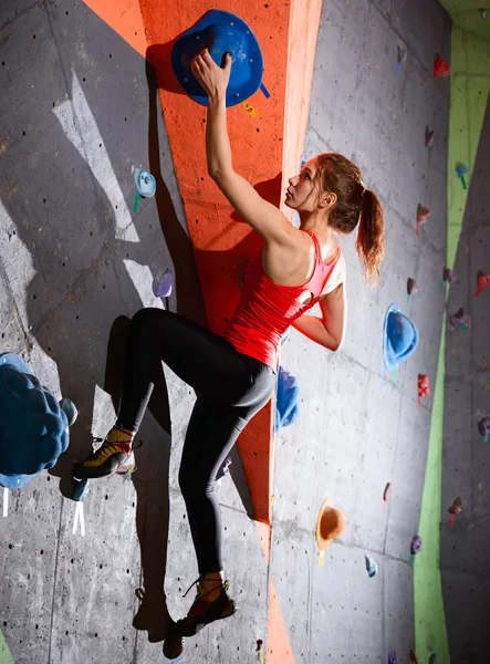 年轻活跃的妇女在五颜六色的人造岩石上攀爬健身房。极限运动和室内攀岩概念 — 图库照片