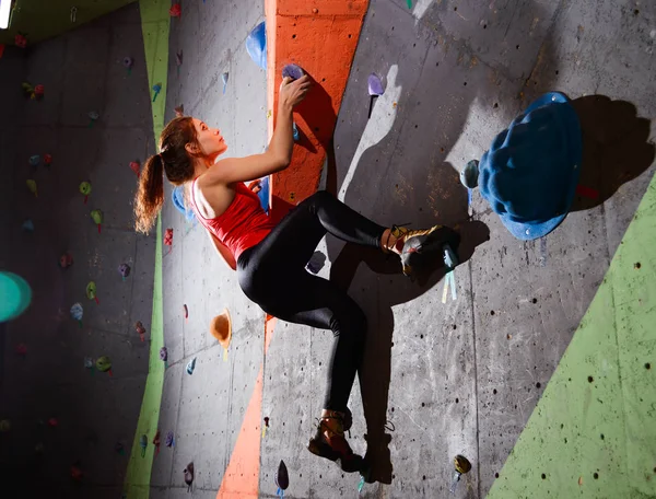 Giovane donna attiva che bouldering sulla roccia artificiale variopinta nella palestra di arrampicata. Sport estremi e concetto di arrampicata indoor — Foto Stock