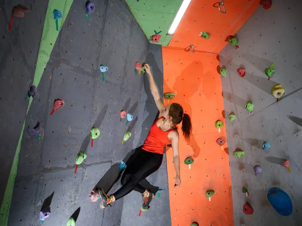 Giovane donna attiva che bouldering sulla roccia artificiale variopinta nella palestra di arrampicata. Sport estremi e concetto di arrampicata indoor — Foto Stock