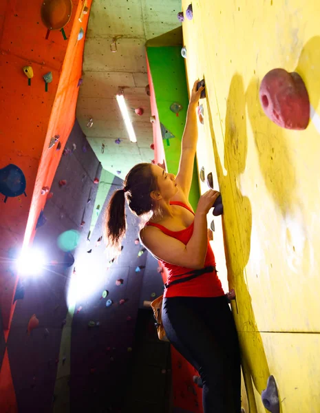 Молода активна жінка, що бореться з барвистою штучною скелею в скелелазіння спортзал. Екстремальний спорт та концепція скелелазіння — стокове фото