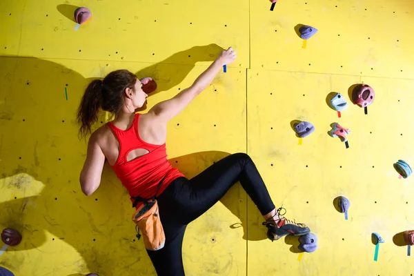 年轻活跃的妇女在五颜六色的人造岩石上攀爬健身房。极限运动和室内攀岩概念 — 图库照片