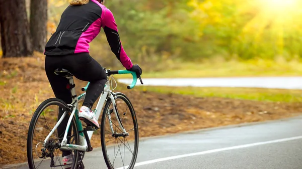 Mujer joven en chaqueta rosa montar en bicicleta por carretera en el parque en la cálida mañana de primavera. Estilo de vida saludable . —  Fotos de Stock