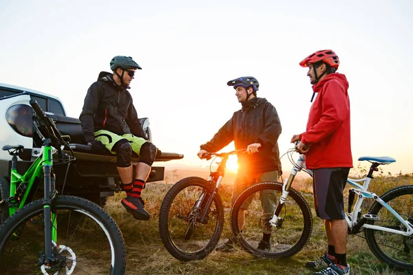 Freunde, die sich nach einer Radtour in den Bergen bei Sonnenuntergang in der Nähe eines Geländewagens ausruhen. Abenteuer und Reisekonzept. — Stockfoto