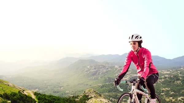 Giovane donna in giacca rosa brillante Riding Road Bicicletta su Mountain Alpine Road. Stile di vita sano e concetto di avventura . — Foto Stock