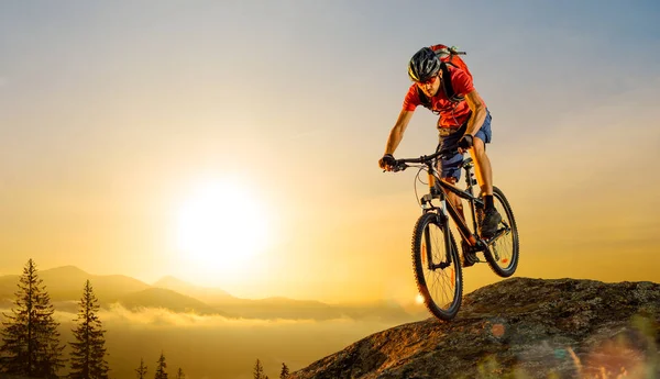 Ποδηλάτης στο κόκκινο ιππασίας το ποδήλατο κάτω από το βράχο με την Ανατολή. Extreme Sport και έννοια ποδήλατο Enduro. — Φωτογραφία Αρχείου