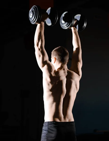 Ritratto di giovane sportivo che solleva manubri pesanti in palestra. Fitness e stile di vita sano Concetto. Illuminazione drammatica — Foto Stock