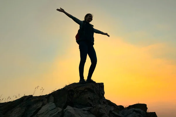 Jeune voyageuse avec sac à dos debout sur le sommet du rocher au coucher du soleil d'été. Concept de voyage et d'aventure. — Photo