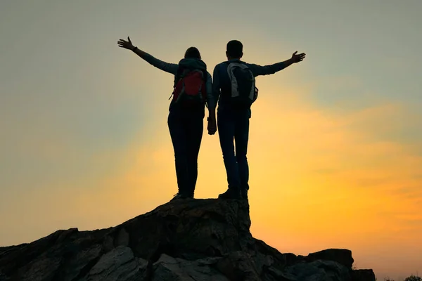 Casal de jovens viajantes com mochila em pé no topo da rocha no pôr do sol de verão. Conceito de viagem e aventura . — Fotografia de Stock