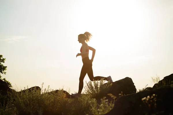 Joven hermosa mujer corriendo en el sendero de la montaña en la puesta del sol caliente del verano. Deporte y estilo de vida activo . — Foto de Stock