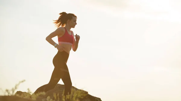 Joven hermosa mujer corriendo en el sendero de la montaña en la puesta del sol caliente del verano. Deporte y estilo de vida activo . — Foto de Stock