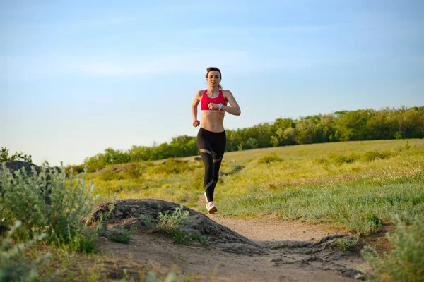 Joven hermosa mujer corriendo en el sendero de la montaña en la noche de verano caliente. Deporte y estilo de vida activo . — Foto de Stock