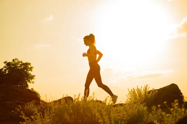 Joven hermosa mujer corriendo en el sendero de la montaña en la puesta del sol caliente del verano. Deporte y estilo de vida activo . — Foto de Stock