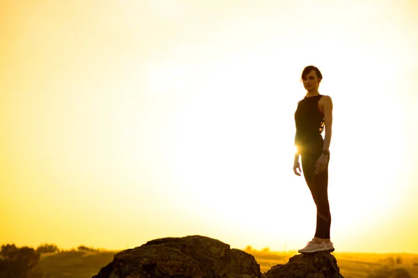 Jonge vrouw staande op de rots bij hete mooie zomer zonsondergang. Avontuur en gezond actief Lifesyle concept. — Stockfoto