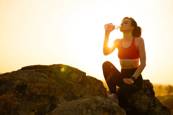 Mulher descansando e bebendo água depois de correr ao ar livre. Treino no pôr-do-sol quente do verão. Esporte e Vida Ativa Saudável . — Fotografia de Stock