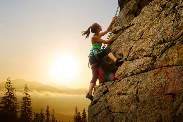 Hermosa mujer escalando en la roca en Foggy Sunset en las montañas. Aventura y concepto de deporte extremo —  Fotos de Stock