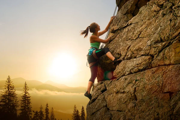 Vacker kvinna klättring på klippan vid dimmigt solnedgång i bergen. Äventyrs-och extrem sport koncept — Stockfoto