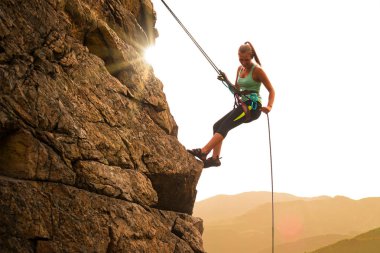 Beautiful Woman Climbing on the Rock at Foggy Sunset in the Mountains. Adventure and Extreme Sport Concept clipart