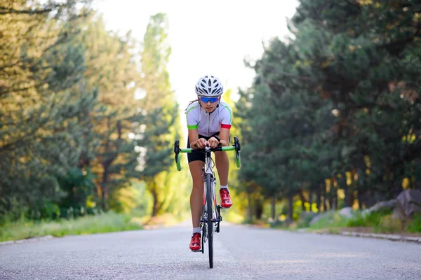 Eine junge Radfahrerin ist an heißen Sommertagen auf der freien Straße im Wald mit dem Rennrad unterwegs. Konzept eines gesunden Lebensstils. — Stockfoto