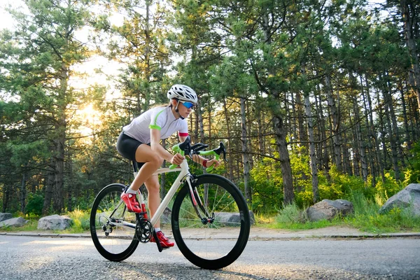 Eine junge Radfahrerin ist an heißen Sommertagen auf der freien Straße im Wald mit dem Rennrad unterwegs. Konzept eines gesunden Lebensstils. — Stockfoto