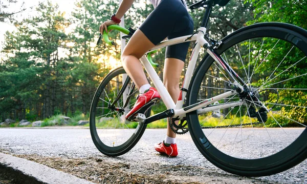 Eine junge Radfahrerin ist an heißen Sommertagen auf der freien Straße im Wald mit dem Rennrad unterwegs. Konzept eines gesunden Lebensstils. — Stockfoto