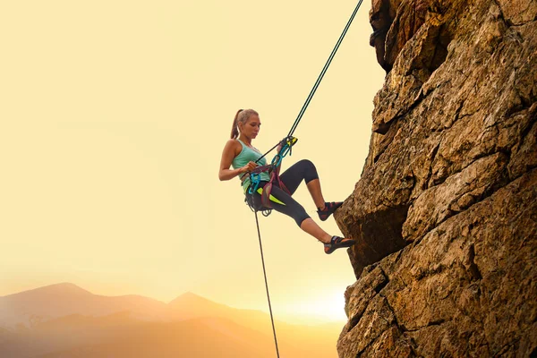 Gyönyörű nő hegymászás a szikla a ködös naplemente a hegyekben. Kalandtúra és extrém sportok koncepció — Stock Fotó