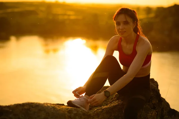 Νεαρή αθλητική γυναίκα δέσιμο παπούτσια τρέξιμο και προετοιμασία για μονοπάτια τρέξιμο στο ηλιοβασίλεμα. Υγιεινός τρόπος ζωής και Αθλητισμός concept. — Φωτογραφία Αρχείου